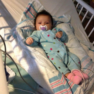 GracieJo in a hospital bed, wearing pajamas and hooked up to a medical device.