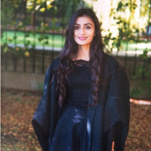 Young Woman With Long Hair Wearing A Black Dress And Gown, Standing Outdoors With A Soft Smile.