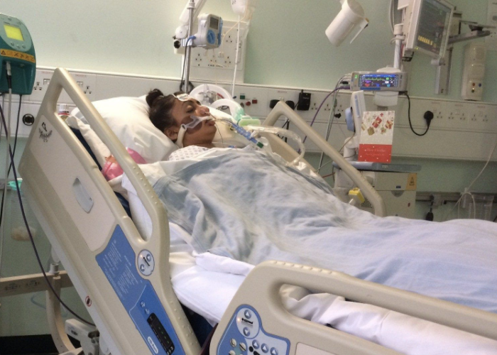 Patient lying unconscious in a hospital bed, connected to a ventilator and surrounded by medical equipment in an ICU.