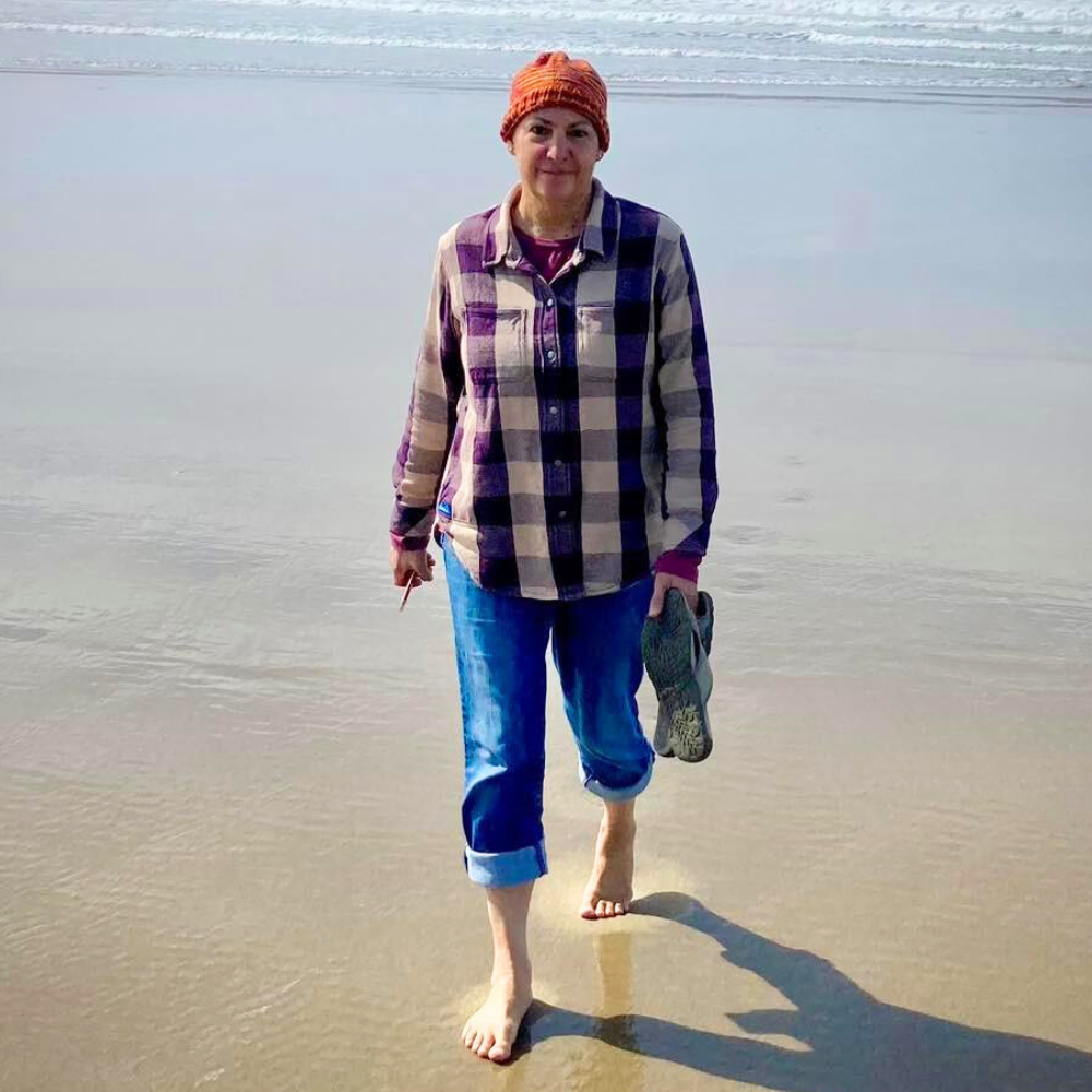 A woman with an orange cap and purple plad shirt on the beach.