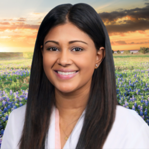 A Photo Of A South Asian Woman With Long, Straight Hair And A Friendly Smile Sitting In Front Of A Field Of Flowers.