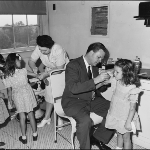 A Black And White Photo From The 1940s Of Two Children Receiving Smallpox Vaccines.